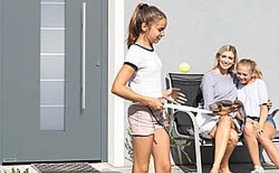 Spielende Kinder mit Mutter vor einer Haustür